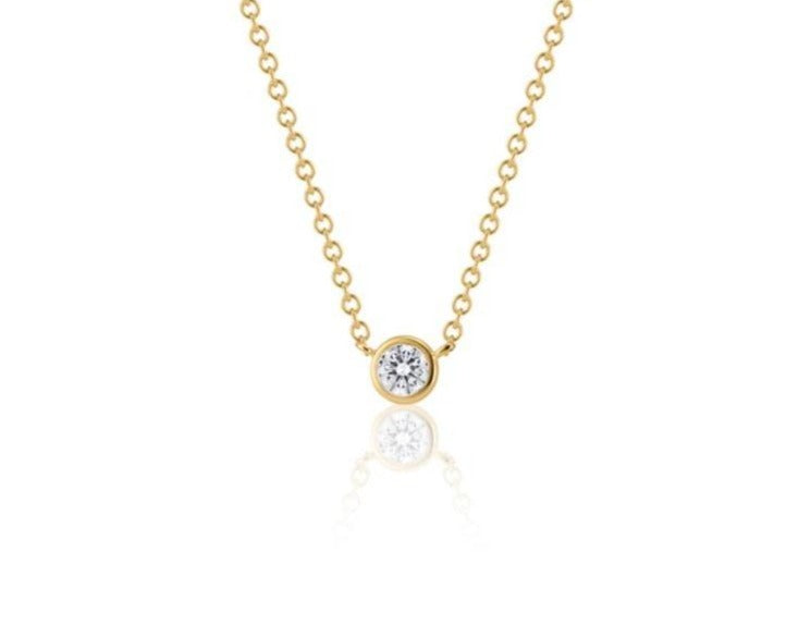 Front view of a round brilliant cut diamond necklace sitting upright. The diamond is set in a yellow gold round bezel setting. The yellow gold round-link chain connects at each side of the bezel setting. 
