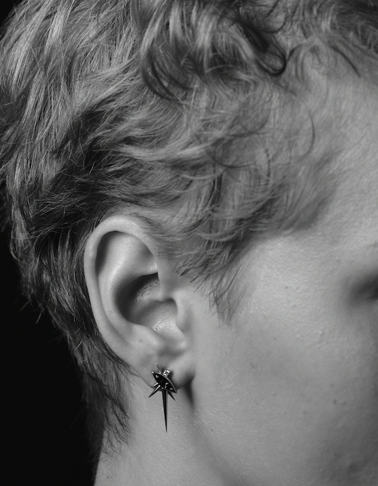 Side view of a person's ear with a spider-shaped earring. Black and white image.
