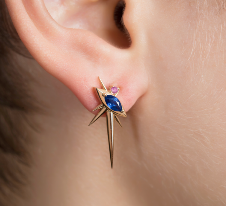 Close-up of an ear with a star-shaped earring featuring a blue and pink sapphire gemstone.