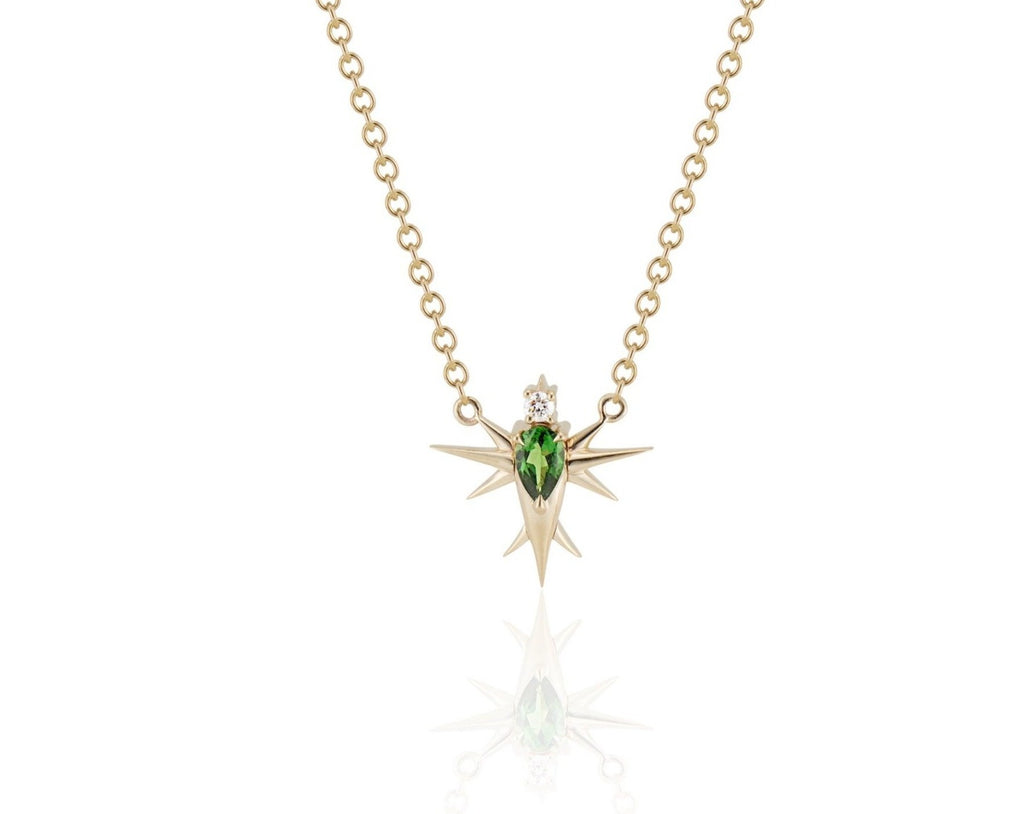 Front view of abstract bird pendant necklace connected to a yellow gold round-link chain. A pear-shaped tsavorite stone forms the bird’s body, topped with a round diamond head. Yellow gold spikes extend from the body to form wings and a tail. 
